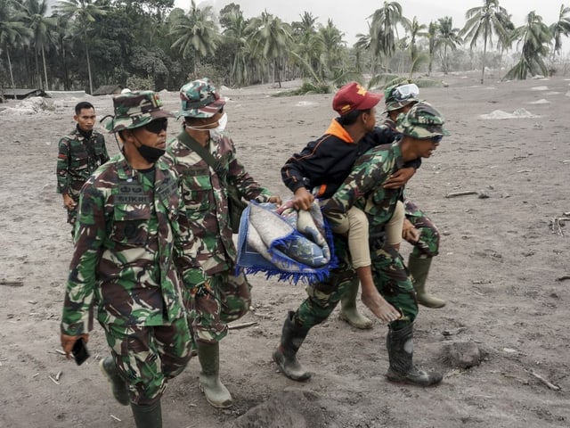 Army personnel evacuate a villager from an area hit by the eruption of Semeru volcano.