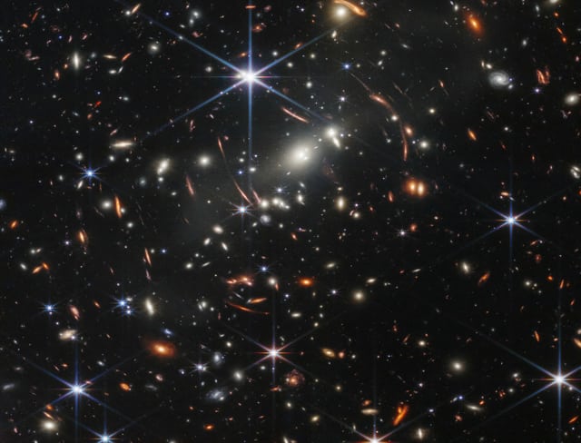 Many glowing stars and galaxies of different colors can be seen on a black background.