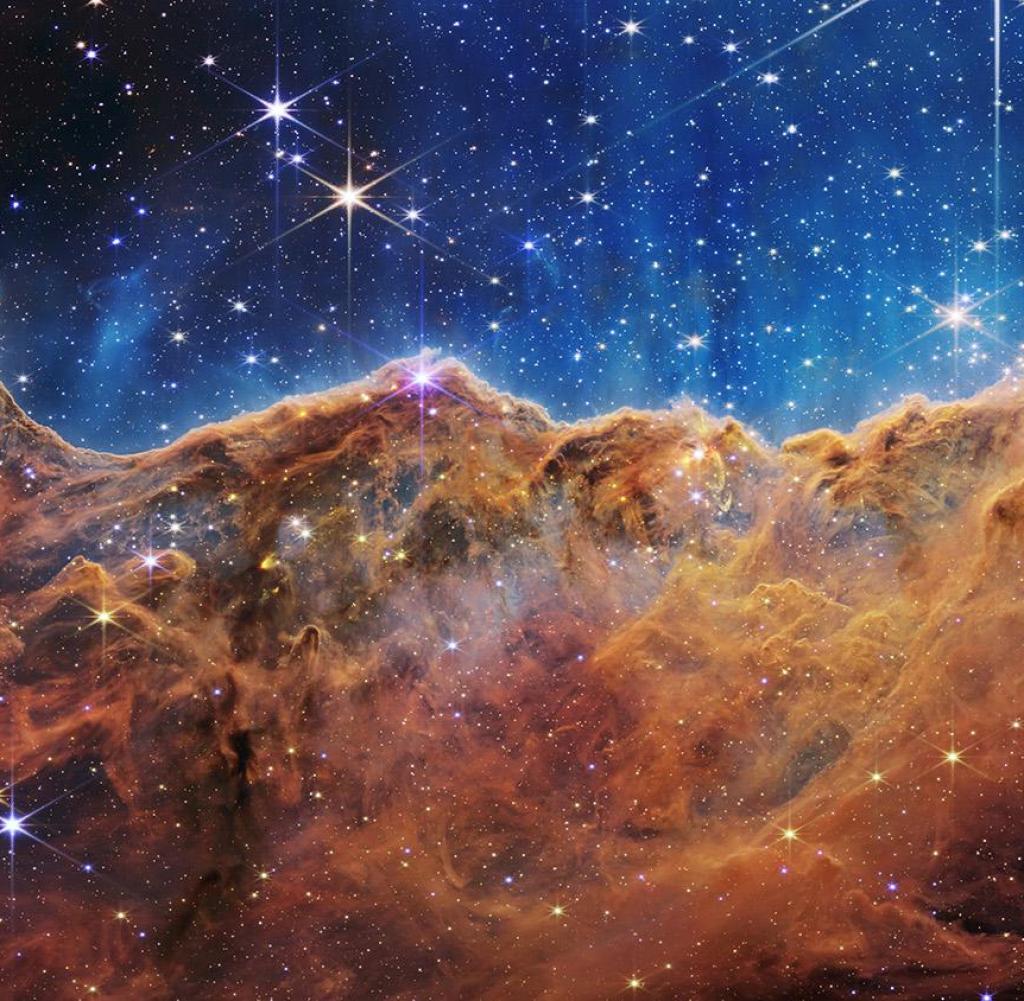 What looks a lot like rocky mountains on a moonlit evening is actually the edge of the nearby and young star-forming region NGC 3324 in the Carina Nebula.  This image was captured in infrared light by the Near Infrared Camera (NIRCam) on the NASA/ESA/CSA James Webb Space Telescope and reveals previously obscured regions of star birth.  The region is called the Cosmic Slope, and it's actually the edge of a giant gas cavity within NGC 3324, about 7,600 light-years away.  The cavernous region of the nebula has been sculpted by intense ultraviolet radiation and stellar winds from young, extremely massive and hot stars in the center of the bubble, above the region shown in this image.  The high-energy radiation from these stars sculpts the nebula's wall by slowly eroding it.  With unparalleled accuracy and sensitivity, NIRCam unveils hundreds of previously hidden stars, and even many background galaxies.  Several notable features in this image are described below.  