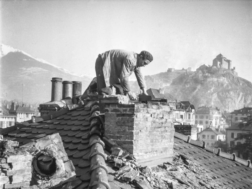 A man gets on his knees on the roof of a destroyed house in Sion.