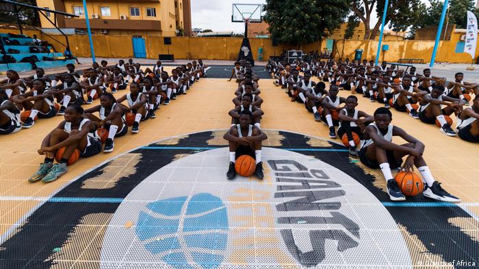 Members of the Africa Giants youth camp in Ouagadougou, Burkina Faso, sit in rows on the floor of the training hall, each basketball player holding in front of his body.